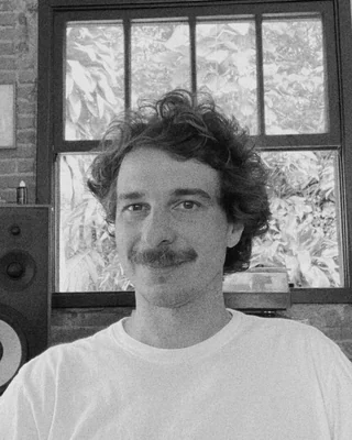 retrato de felipe duarte sorrindo, de camiseta branca, no estúdio